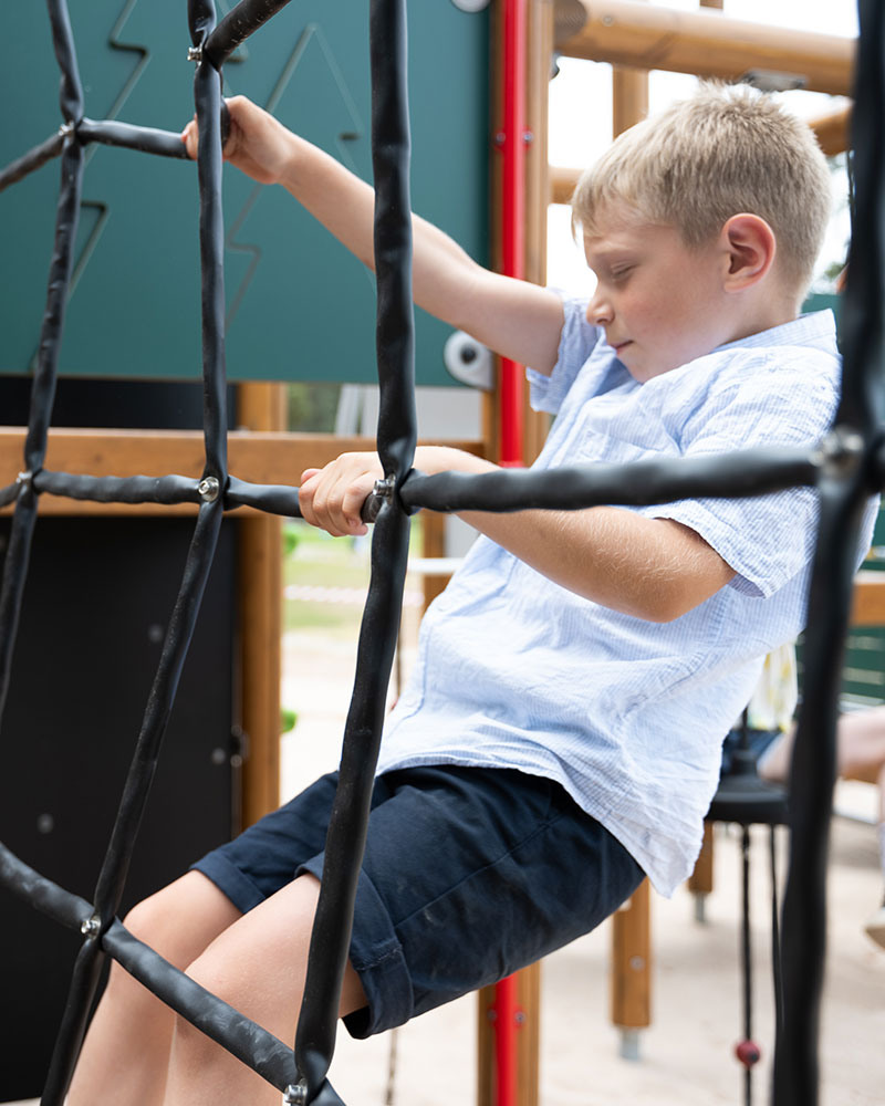 Ein kleiner Junge klettert konzentriert über einen Netzhindernisparcours auf einem Spielplatz.